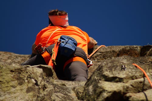 Person in Orange Shirt Climbing Rock during Daytime