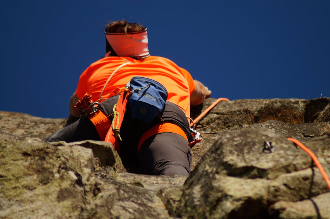 Free Person in Orange Shirt Climbing Rock during Daytime Stock Photo