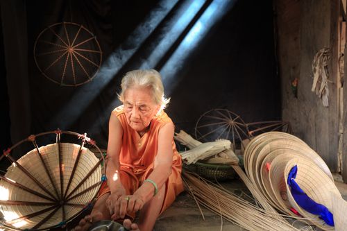 Free Senior woman crafting straw hats in natural light, showcasing traditional artisan skills. Stock Photo
