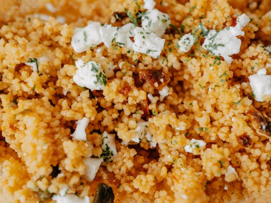 Close view of orange-tinted couscous topped with crumbled feta, parsley and sun-dried tomato