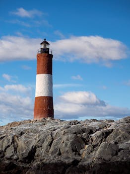 Explore the iconic red and white lighthouse in Ushuaia, Argentina against a picturesque blue sky.