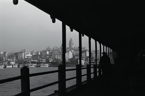 A black and white photo of a pier with a city in the background