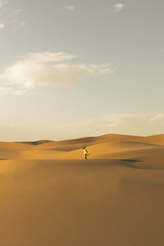 Lone person walking among sand dunes in the Moroccan Sahara Desert during the day.