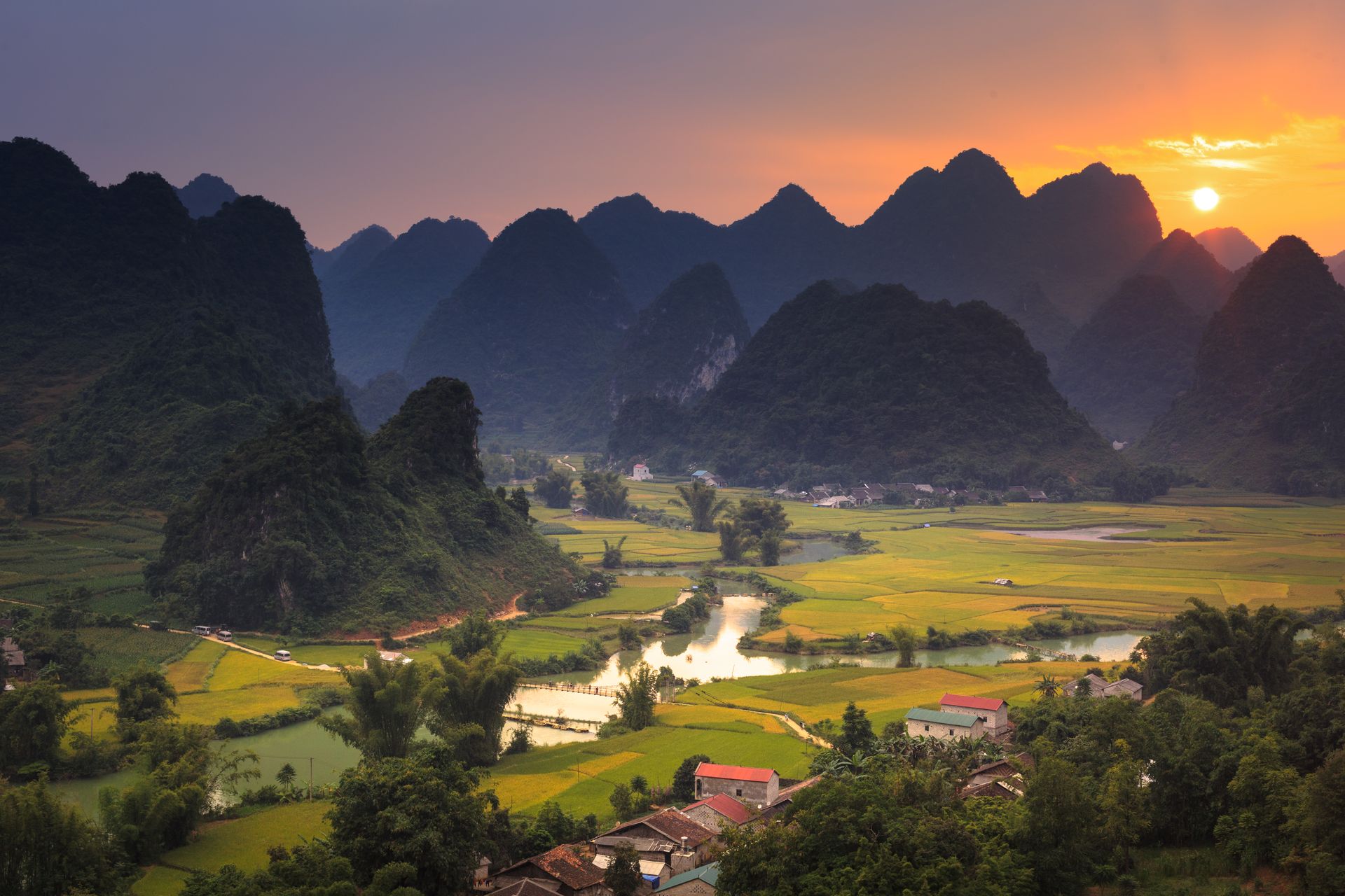 A tranquil scene capturing the sunset over lush fields and towering mountains, depicting peaceful rural life.