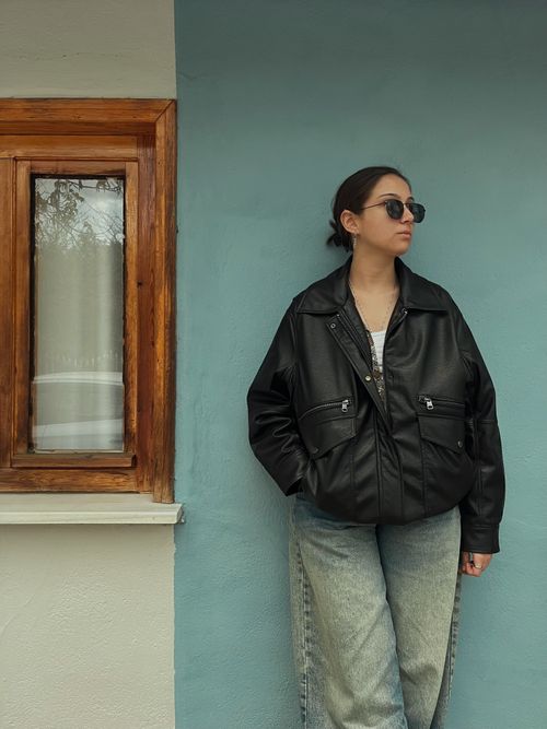 Free Stylish woman in sunglasses and leather jacket poses against a blue wall in Edirne, Türkiye. Stock Photo