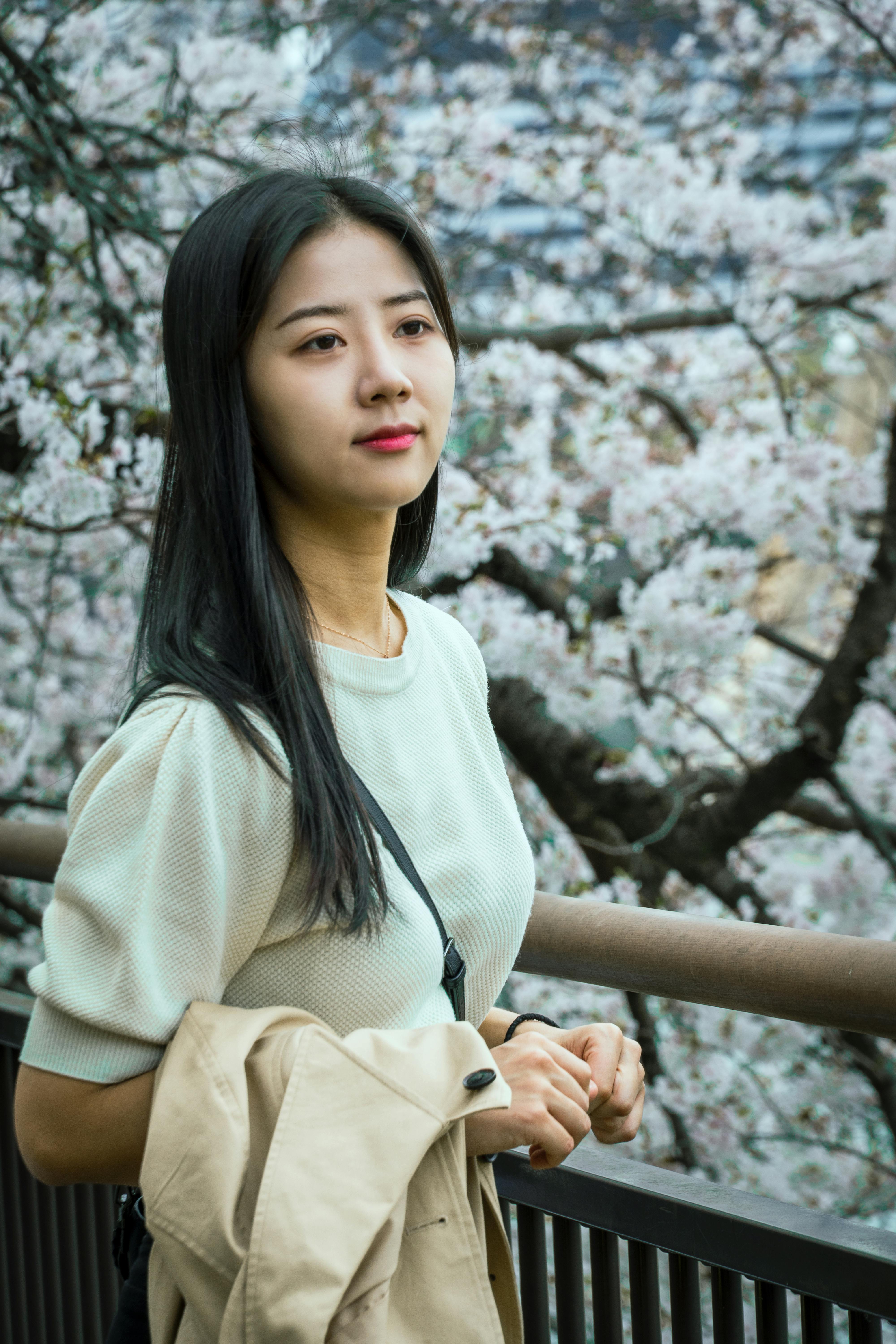 Asian woman standing by a cherry blossom tree in a Japanese park, enjoying springtime.