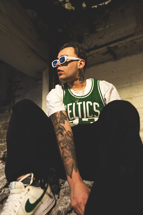 A man with tattoos and glasses sitting on a ledge