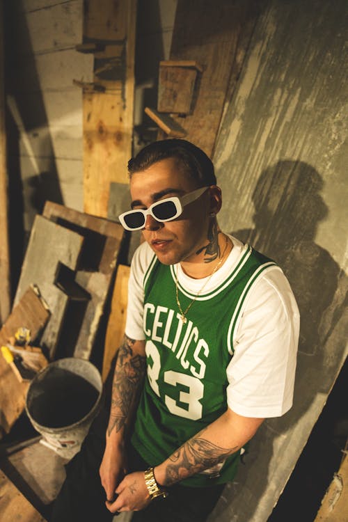 A man with tattoos and glasses sitting on a wooden floor