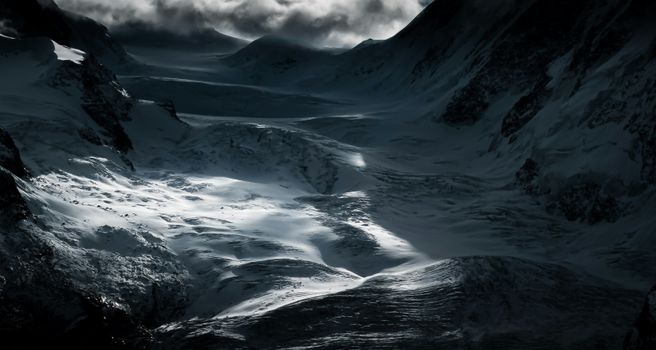 Stunning view of a snow-covered mountain valley under dark, dramatic skies in winter.