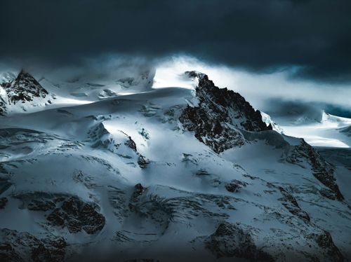 Free A breathtaking view of snow-covered mountain peaks under dramatic evening skies. Stock Photo