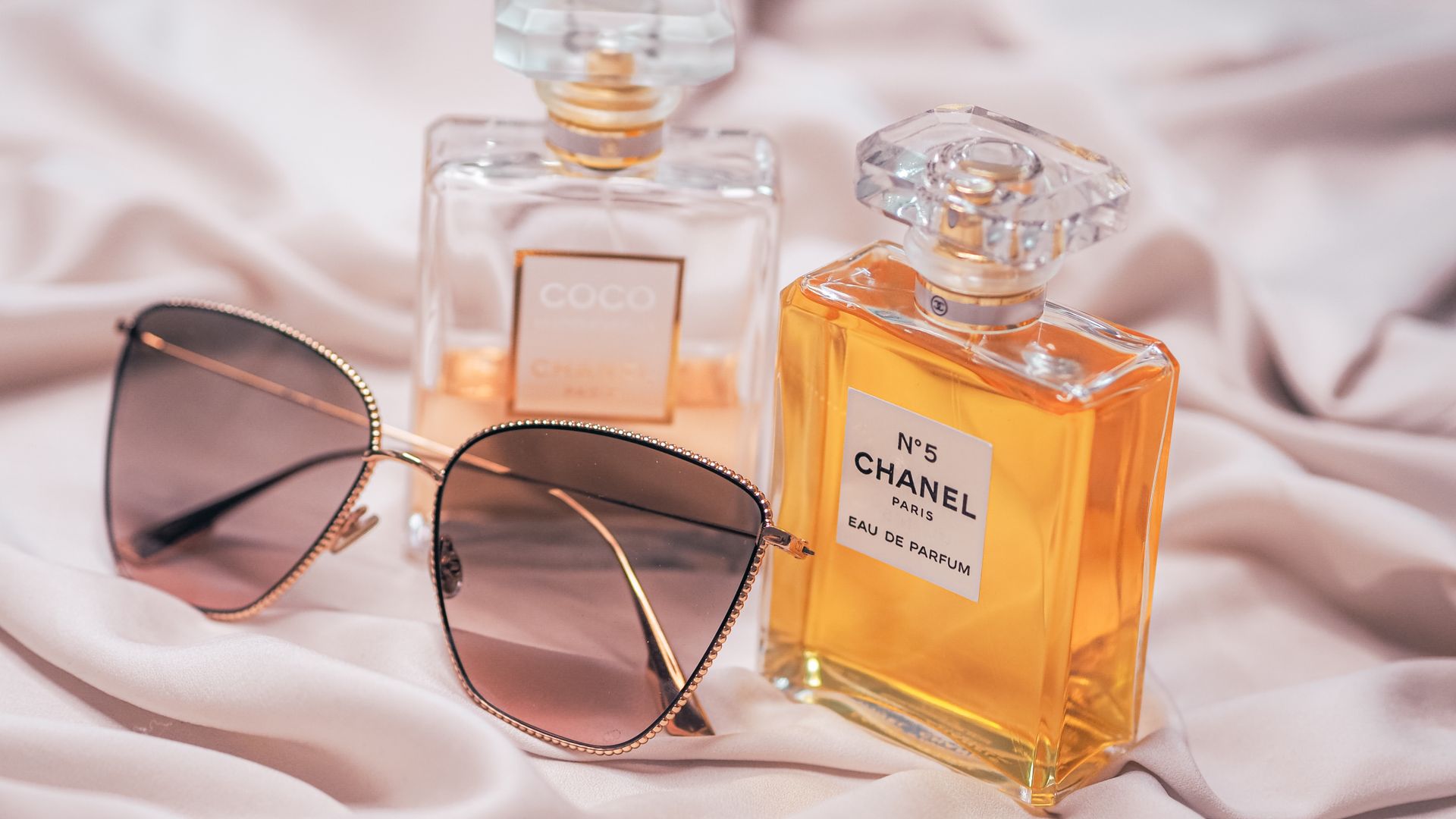 Chanel perfume bottles and stylish sunglasses on a silky surface, perfect for luxury fashion marketing.