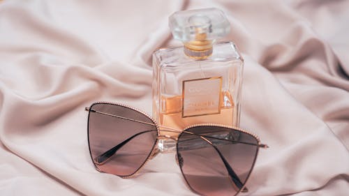 A pair of sunglasses and perfume on a bed