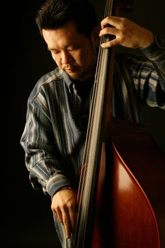 Focused musician playing double bass in a studio setting against a dark background.