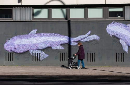 A woman walking past a mural of two fish