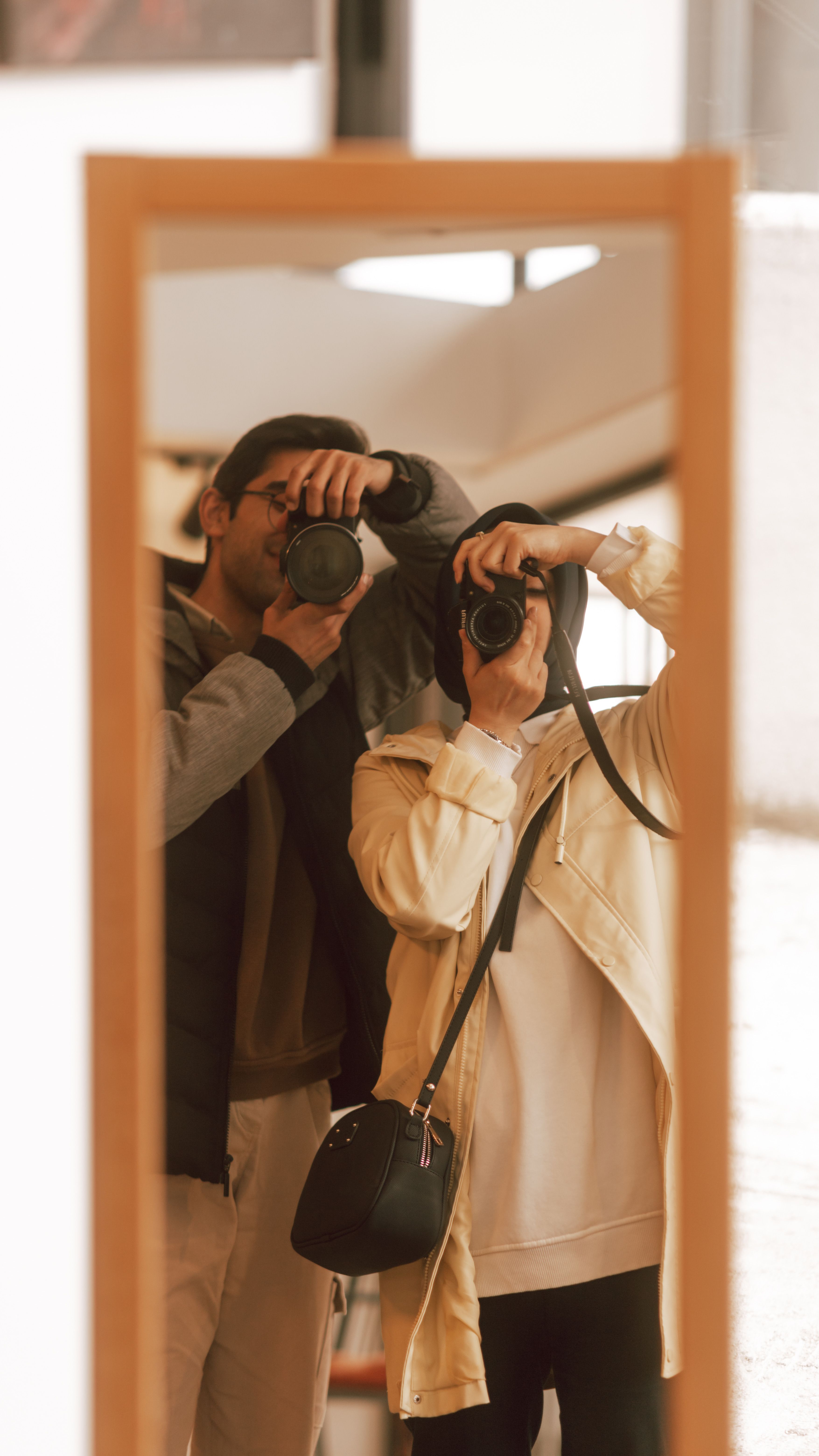 Two individuals taking pictures in a mirror, showcasing fashion and photography style.