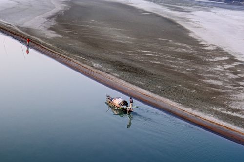 Free Aerial view of a lone fisherman in a traditional boat on a tranquil riverbend, serene landscape. Stock Photo