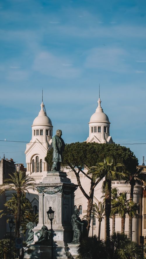 Free A historic statue sits before dual-towered church architecture under a clear blue sky. Stock Photo