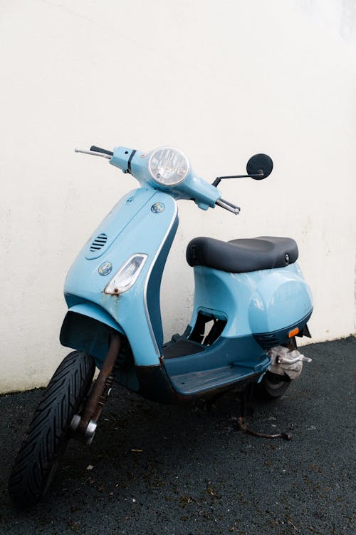 A blue moped parked against a white wall