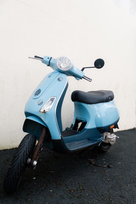 A stylish blue scooter parked on asphalt against a white wall, creating a minimalist contrast.