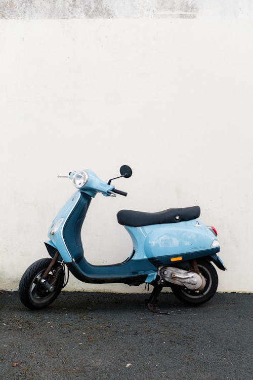 A blue moped parked against a white wall