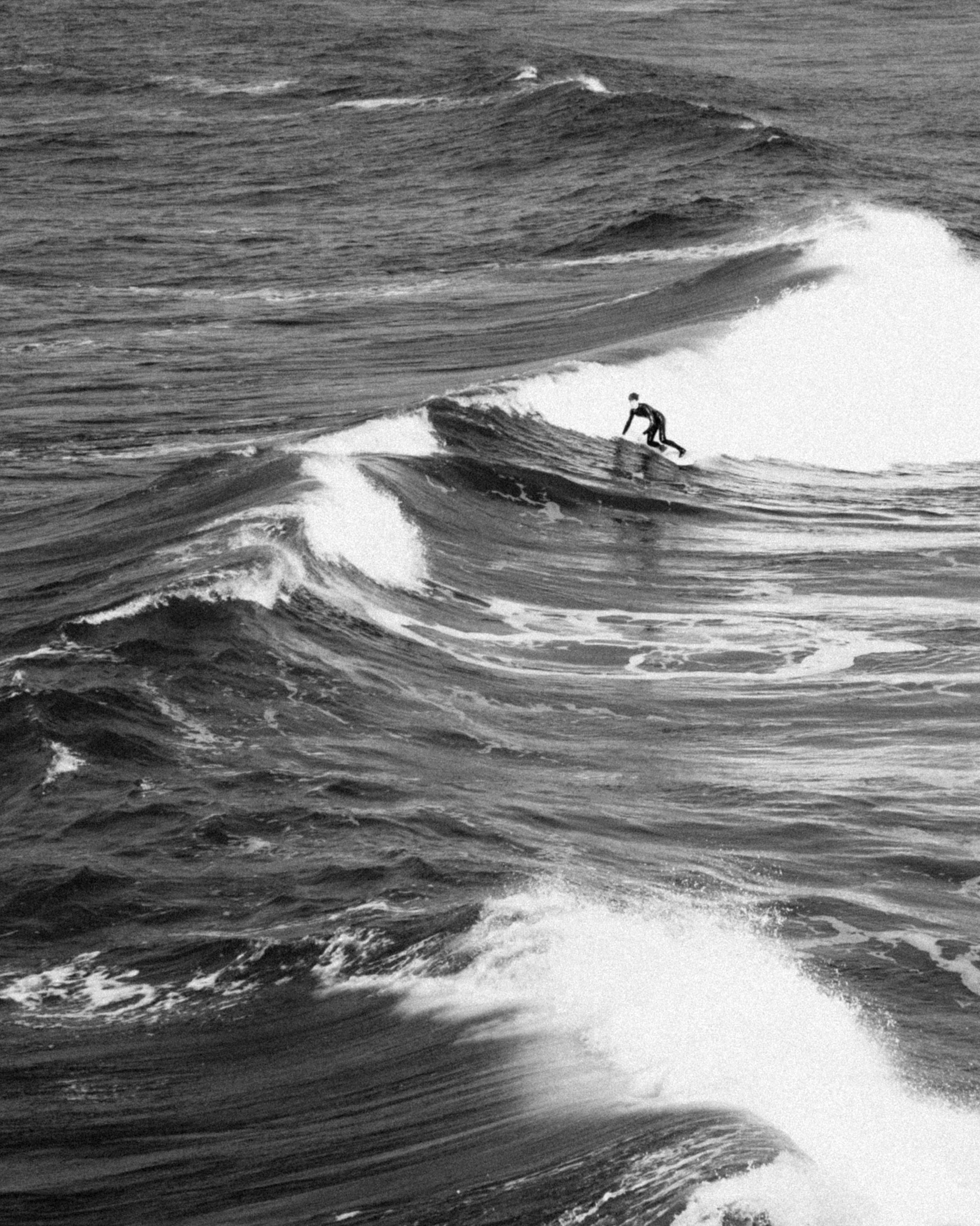 A lone surfer rides towering ocean waves in a captivating black and white landscape.
