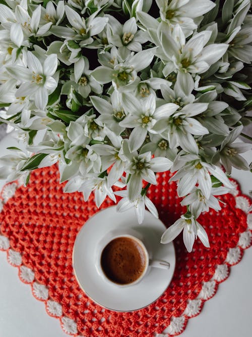 A cup of coffee and flowers on a red and white crocheted doily