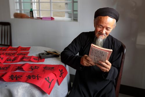 Free An elderly man reading book with calligraphy paper, embodying tradition and wisdom. Stock Photo