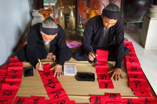 Free Elderly Asian men practicing traditional calligraphy indoors on red paper. Stock Photo