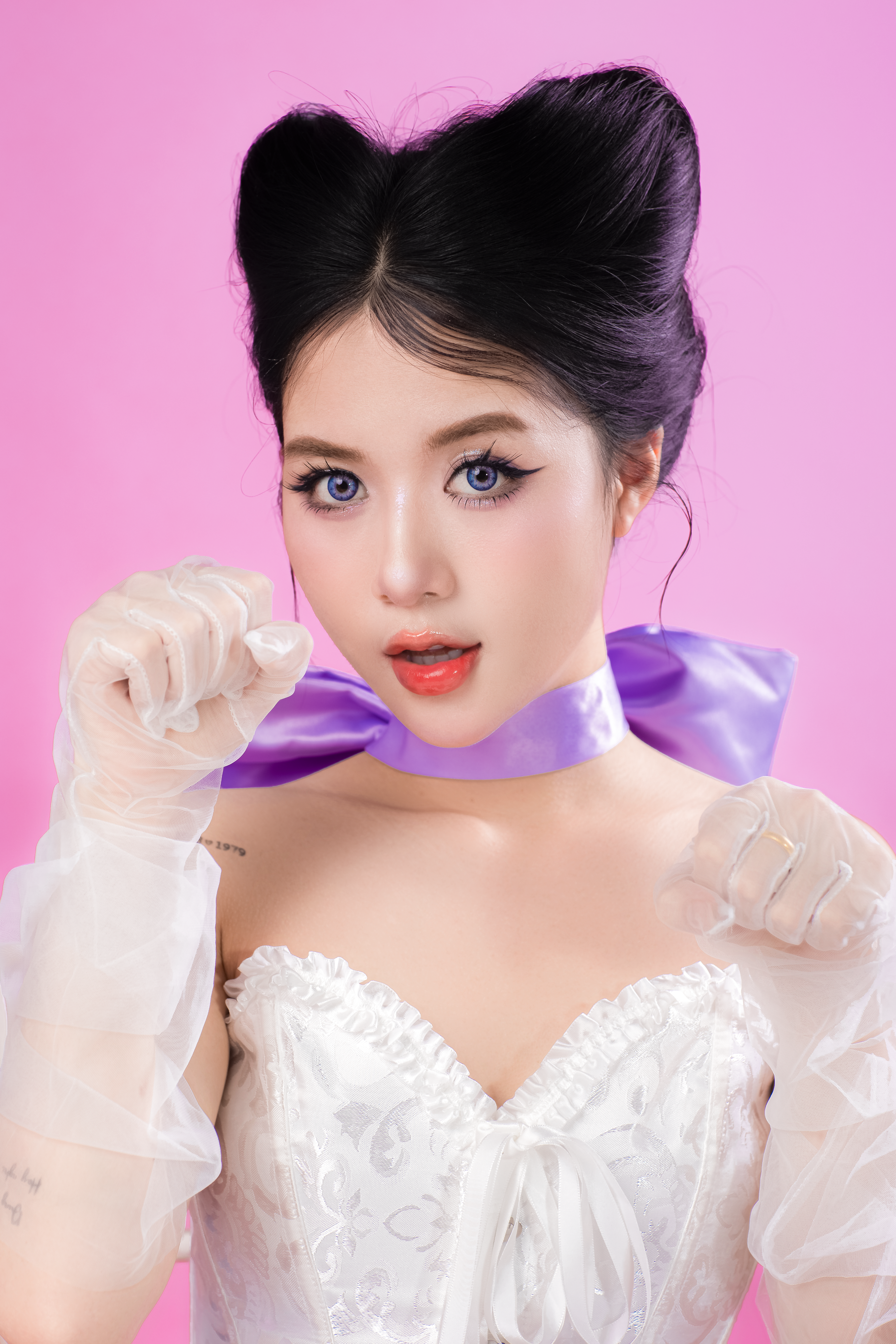 Young woman in fashionable white dress posing against pink backdrop.