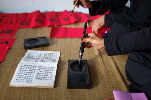 Free Close-up of adults practicing calligraphy on bamboo mat with ink and brush. Stock Photo