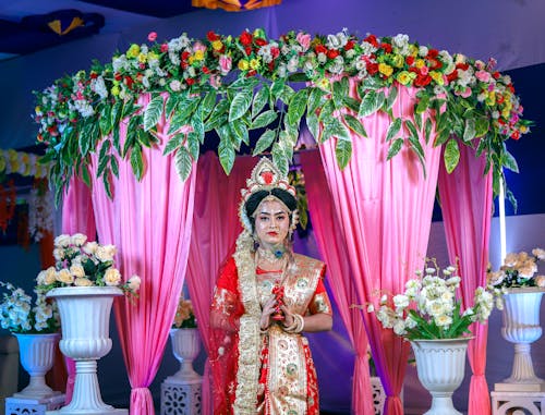 A woman in a traditional indian dress standing in front of a floral arch