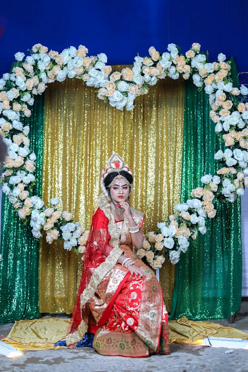 A woman in a red and gold sari sitting on a chair