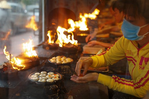 Street vendor carefully cooks traditional Asian dish over open flames, showcasing vibrant street food culture.