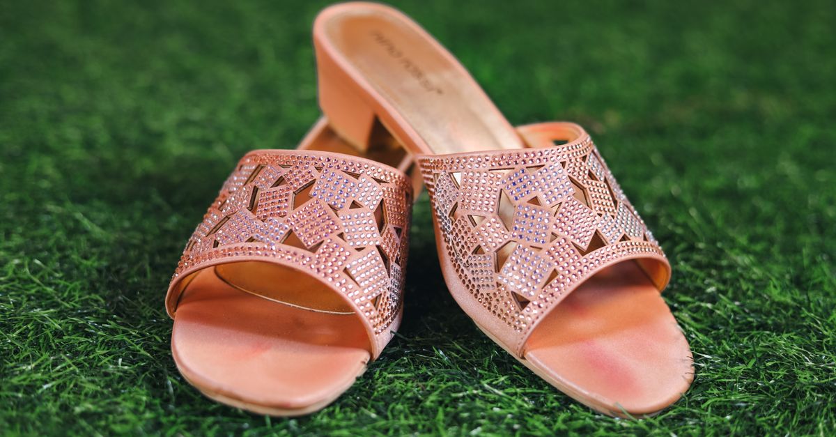 Stylish pink slip-on sandals with intricate designs placed on lush green grass, showcasing fashion elegance.