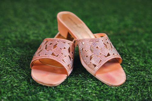 Free Stylish pink slip-on sandals with intricate designs placed on lush green grass, showcasing fashion elegance. Stock Photo