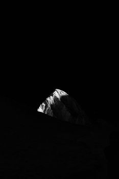 A dramatic black and white image of a single mountain peak illuminated at night.
