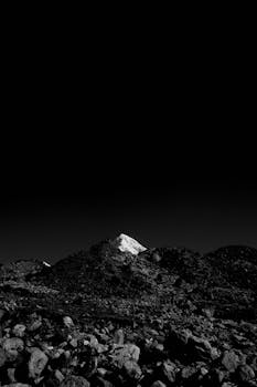 A striking black and white image of a mountain peak under a vast dark sky, emphasizing contrast.