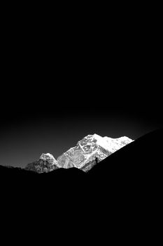 Black and white photo of a snow-covered mountain peak against a dark sky.