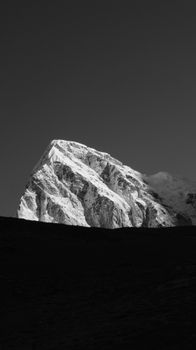 Striking black and white image of a snowcapped mountain peak against a clear sky, showcasing nature's grandeur.
