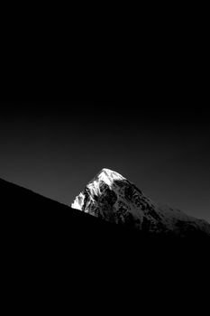 Striking black and white image of a snow-covered mountain peak under a dark sky.