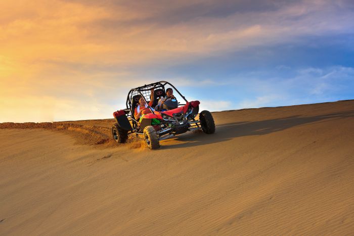 Buggy rouge sur une dune au coucher du soleil
