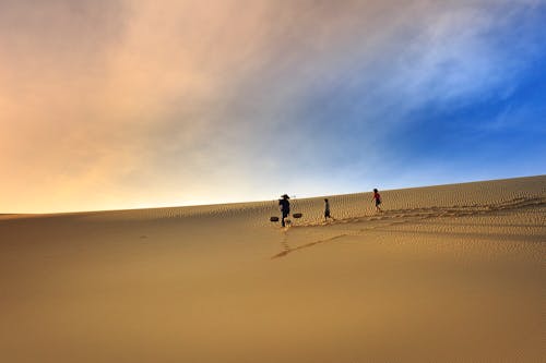 Фотография силуэта трех человек, идущих по песку