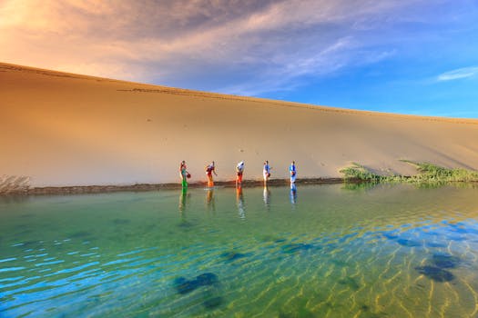四个身着传统服装的人走过一片宁静的沙漠绿洲，清澈的蓝天倒映在水中