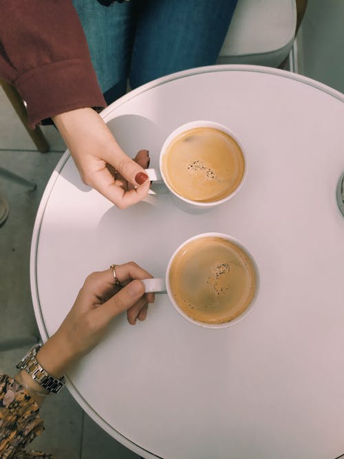 Free Two people holding coffee cups at a table Stock Photo