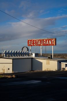 Old restaurant sign atop a deserted building under a clear blue sky.