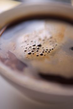 Artistic close-up of a steaming coffee cup with frothy bubbles on top.