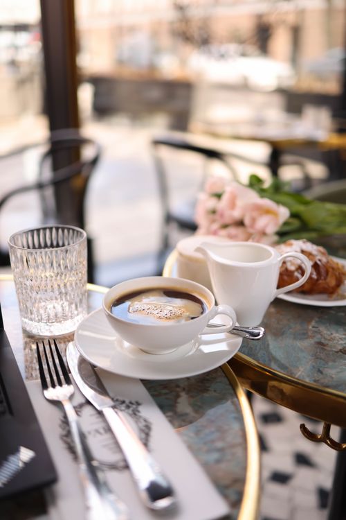 Free A warm morning coffee setup in a stylish café with pastries and pink flowers on the table. Stock Photo