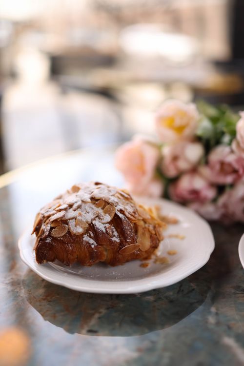 Free Delicious almond croissant on a plate beside pink flowers, perfect for breakfast delight. Stock Photo
