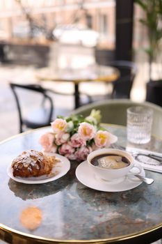 A refined café setting with coffee, croissant, and flowers on a marble table.