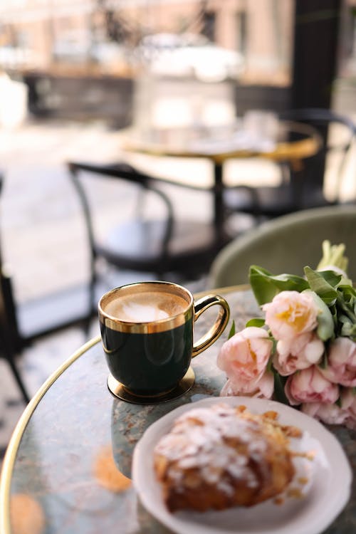 Free A coffee cup and pastry on a table next to flowers Stock Photo